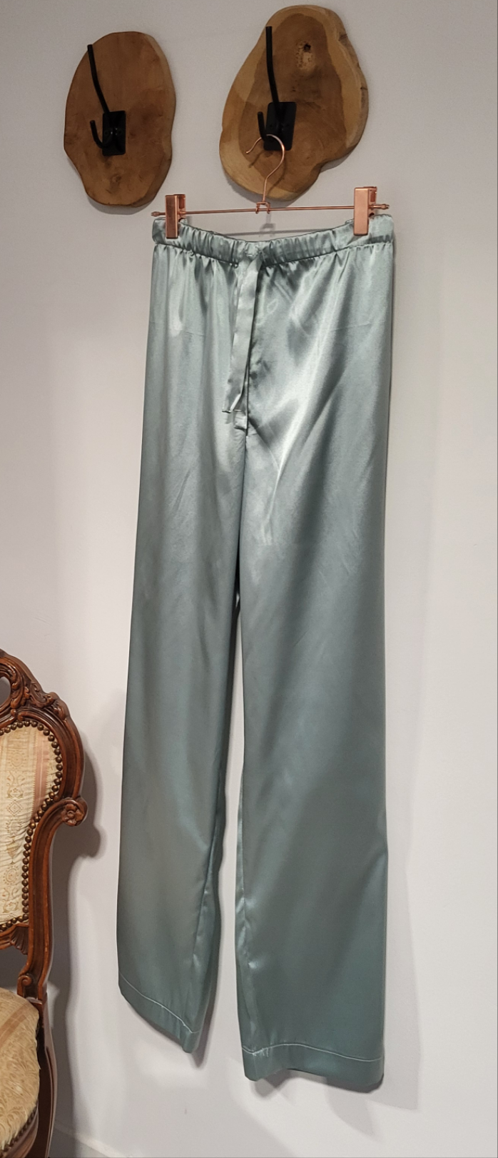 Close-up van een zijdezachte satijnen Aurora pyjama in zacht glanzend materiaal, gedragen door een vrouw die ontspannen zit, met subtiele details en een elegante pasvorm. Aurora pyjama  met spaghettitop, lange broek of short.


